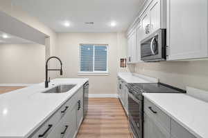 Kitchen featuring light wood-type flooring, appliances with stainless steel finishes, sink, and light stone counters