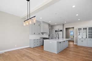 Kitchen featuring light hardwood / wood-style flooring, decorative light fixtures, sink, fridge, and a kitchen island with sink