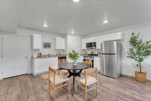 Kitchen with white cabinets, appliances with stainless steel finishes, light hardwood / wood-style floors, and sink