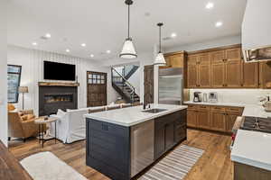 Kitchen featuring light wood-type flooring, decorative light fixtures, a premium fireplace, sink, and decorative backsplash