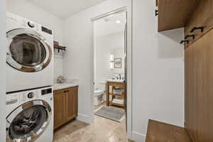 Laundry room with stacked washer and dryer, cabinets, and light tile patterned flooring