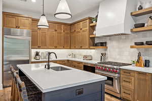 Kitchen with built in appliances, backsplash, an island with sink, premium range hood, and sink