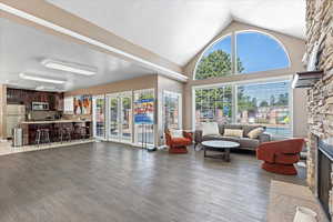 Living room featuring light wood-type flooring, a textured ceiling, high vaulted ceiling, and a stone fireplace