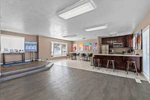 Kitchen featuring a textured ceiling, appliances with stainless steel finishes, kitchen peninsula, light tile patterned flooring, and a breakfast bar