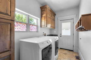 Clothes washing area with washing machine and dryer, light tile patterned floors, and sotrage cabinets