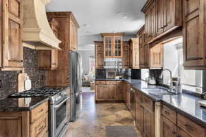 Kitchen with custom range hood, appliances with stainless steel finishes, backsplash, tile patterned flooring, and sink