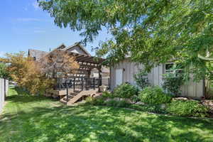 Rear view of property featuring a pergola, a wooden deck, and a lawn