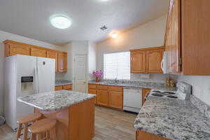 Kitchen with a center island, white appliances, light stone counters, light hardwood / wood-style floors, and lofted ceiling