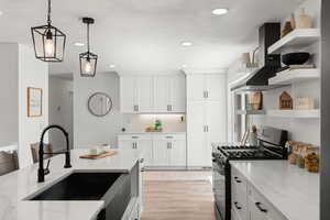 Kitchen with gas range, light stone countertops, decorative light fixtures, light hardwood / wood-style flooring, and sink