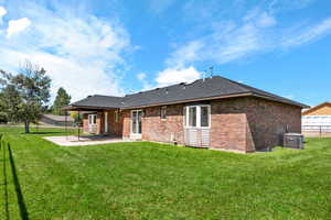 Back of house with cooling unit, a lawn, and a patio area