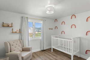 Bedroom with wood-type flooring, a nursery area, and an inviting chandelier