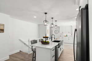 Kitchen with appliances with stainless steel finishes, white cabinetry, a kitchen island with sink, and light hardwood / wood-style flooring