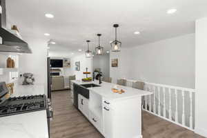 Kitchen with sink, stainless steel gas stove, an island with sink, and light hardwood / wood-style flooring