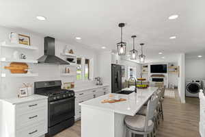 Kitchen featuring a kitchen island with sink, wall chimney exhaust hood, black gas stove, and light hardwood / wood-style floors