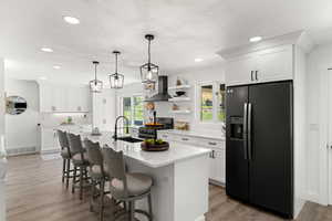 Kitchen with stainless steel electric stove, hardwood / wood-style flooring, an island with sink, and black refrigerator with ice dispenser