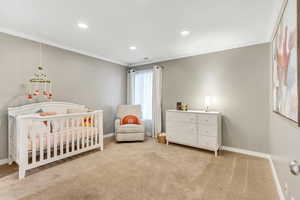 Bedroom with light colored carpet, a nursery area, and ornamental molding