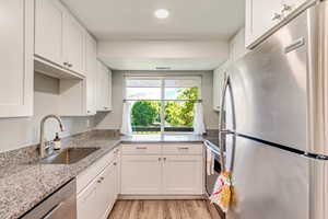 Kitchen featuring light wood-type flooring, appliances with stainless steel finishes, light stone countertops, white cabinetry, and sink