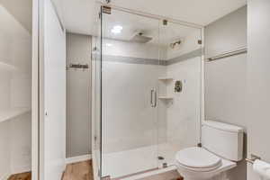 Bathroom featuring a shower with door, toilet, and wood-type flooring