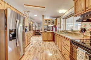 Kitchen with range with electric stovetop, kitchen peninsula, sink, stainless steel refrigerator with ice dispenser, and light hardwood / wood-style floors