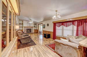 Living room with light hardwood / wood-style flooring, ceiling fan with notable chandelier, and a brick fireplace