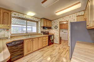 Kitchen with black appliances, light hardwood / wood-style flooring, separate washer and dryer, sink, and lofted ceiling