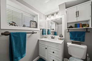 Bathroom with toilet, plenty of natural light, a textured ceiling, and vanity