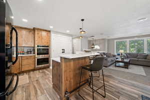 Kitchen featuring hanging light fixtures, stainless steel double oven, light wood-type flooring, black refrigerator, and a breakfast bar