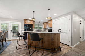 Kitchen with pendant lighting, a wealth of natural light, stainless steel oven, black refrigerator with ice dispenser, and hardwood / wood-style flooring