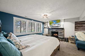 Carpeted bedroom featuring a textured ceiling and a stone fireplace