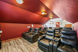 Home theater room with hardwood / wood-style floors, ceiling fan, and vaulted ceiling