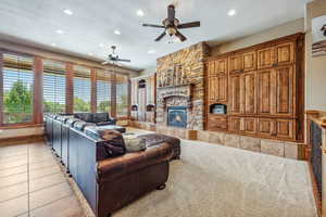 Living room featuring ceiling fan, a stone fireplace, and light tile patterned flooring