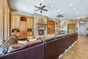 Living room with light tile patterned floors, ceiling fan, and a stone fireplace