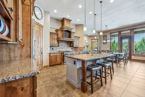 Kitchen with high end stainless steel range, light stone counters, a breakfast bar, light tile patterned flooring, and a large island