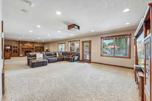 Carpeted living room featuring a textured ceiling and a stone fireplace