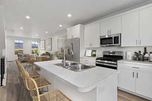 Kitchen with sink, dark hardwood / wood-style floors, appliances with stainless steel finishes, a center island with sink, and white cabinets