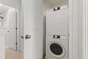 Laundry room featuring light carpet and stacked washer / drying machine