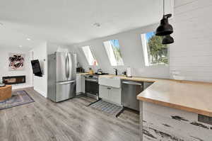 Kitchen featuring light wood-type flooring, pendant lighting, a skylight, sink, and appliances with stainless steel finishes