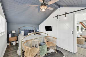 Bedroom with a barn door, ceiling fan, wood-type flooring, and lofted ceiling with beams