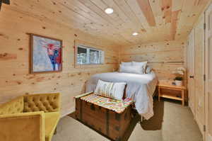 Carpeted bedroom featuring wood walls and wooden ceiling