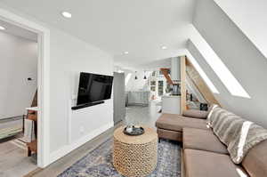 Living room with vaulted ceiling with skylight and light hardwood / wood-style floors