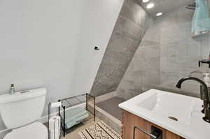 Bathroom featuring toilet, a tile shower, and vanity