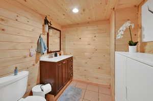 Bathroom with wood ceiling, toilet, wooden walls, and tile patterned floors