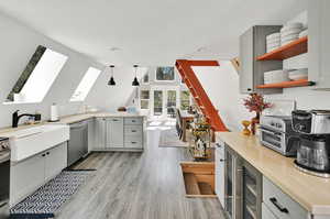 Interior space with gray cabinetry, lofted ceiling with skylight, pendant lighting, light hardwood / wood-style flooring, and stainless steel appliances