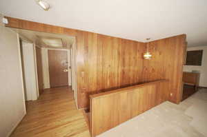 Corridor with light wood-type flooring, a textured ceiling, and wood walls