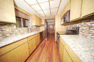 Kitchen with light hardwood / wood-style flooring, stainless steel appliances, sink, decorative backsplash, and light brown cabinets