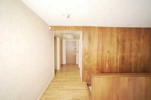 Hallway with light wood-type flooring, a textured ceiling, and wooden walls