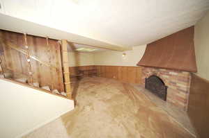 Unfurnished living room with a brick fireplace, wooden walls, and carpet