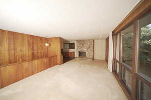 Empty room with wooden walls, a textured ceiling, and a stone fireplace