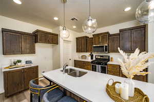 Kitchen featuring a kitchen bar, hanging light fixtures, stainless steel appliances, sink, and hardwood / wood-style flooring