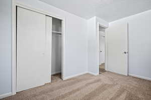 Unfurnished bedroom with a textured ceiling, light colored carpet, and a closet